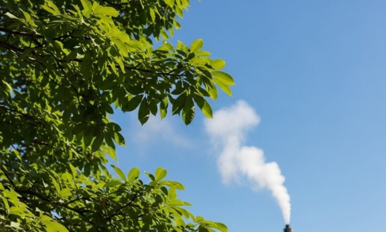 A factory chimney emitting smoke against a clear sky, illustrating industrial activity and air pollution