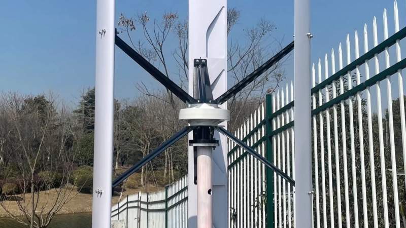 A vertical axis wind turbine stands in a fenced outdoor area