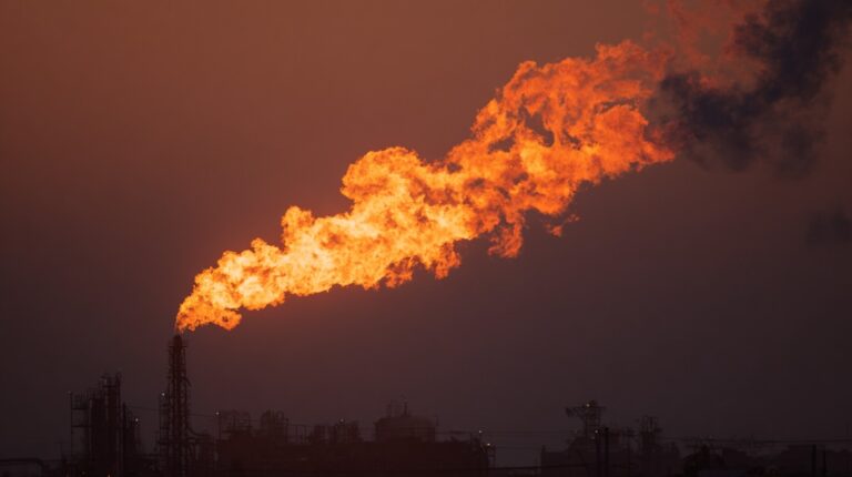 Industrial gas flare burning above an energy facility at night