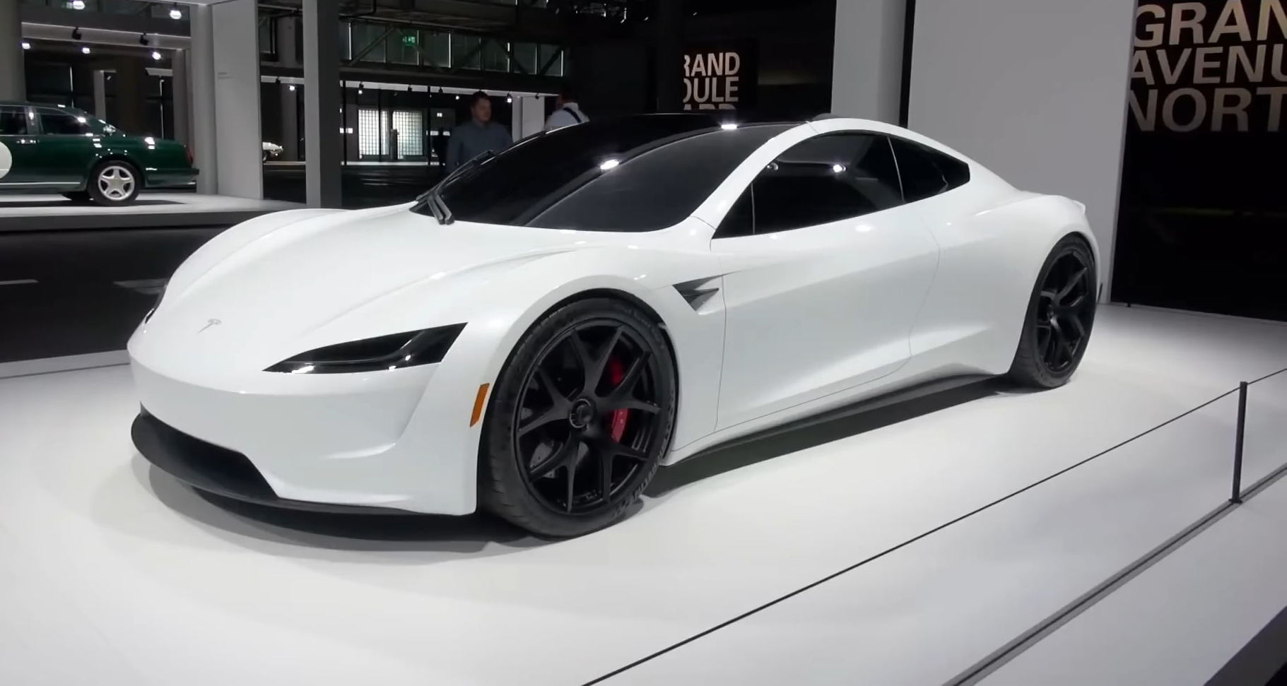 White second-generation Tesla Roadster displayed at an auto show with black wheels and sleek design