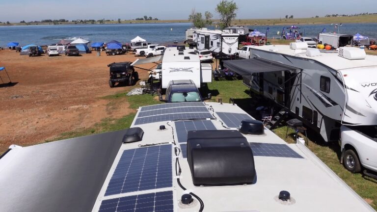 RV with solar panels on the roof parked near other RVs by the water