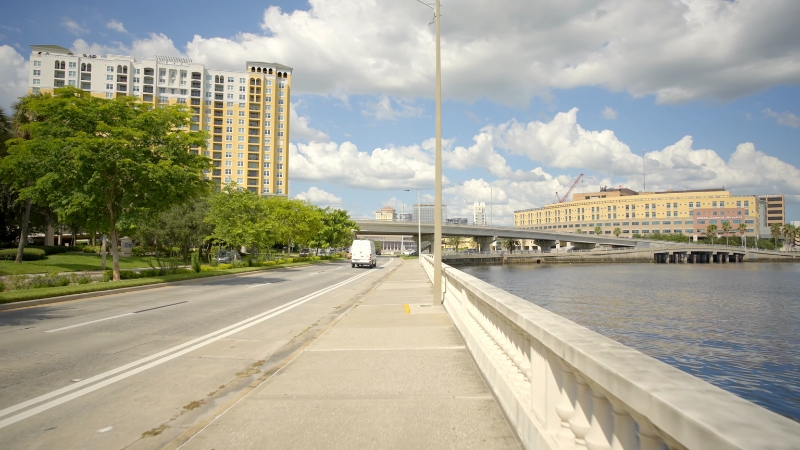 View of Tampa's waterfront, featuring modern buildings, a bridge, and a wide, open sidewalk