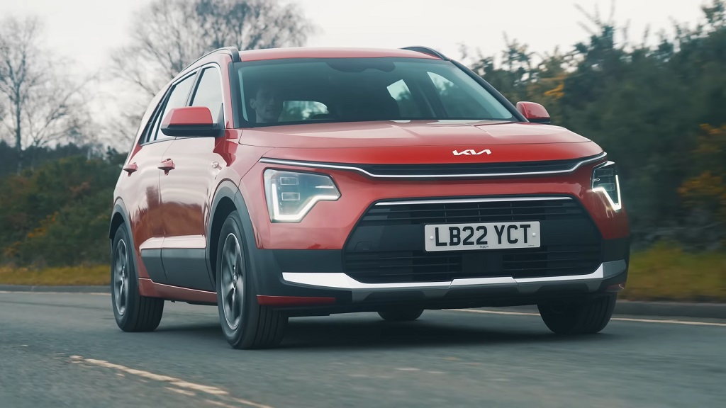 A red Kia Niro Hybrid driving on a rural road, showcasing its modern front design and LED headlights
