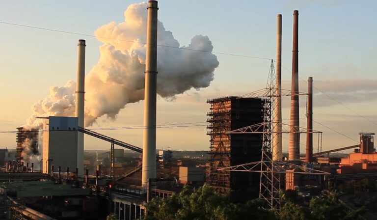 Industrial landscape at sunset, with towering smokestacks releasing plumes of smoke into the dusky sky