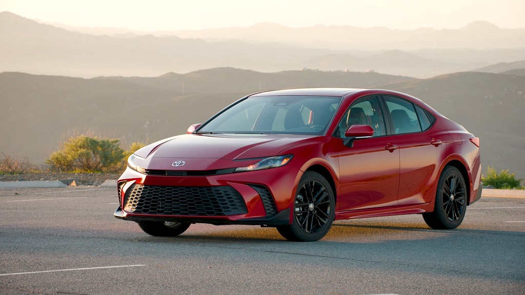 A red Toyota Camry Hybrid parked in a scenic mountain area during sunset, emphasizing its sleek body and aerodynamic lines
