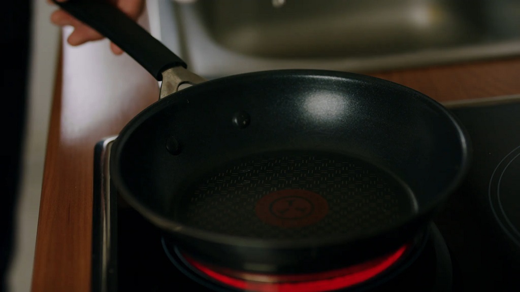 Empty non-stick frying pan heating on an electric stovetop with red glow indicating active burner