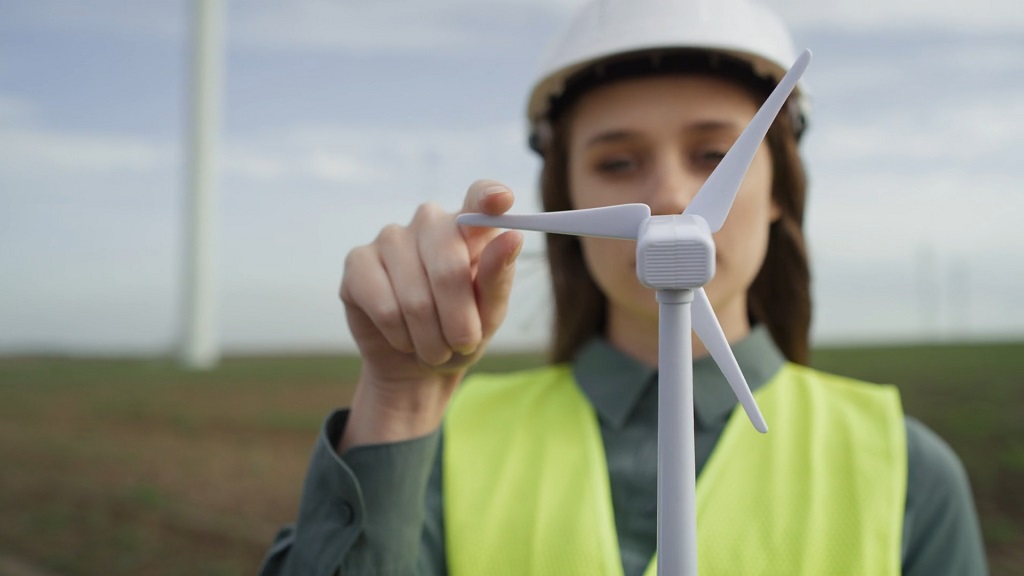 Woman in safety gear inspecting wind turbine model for climate awareness