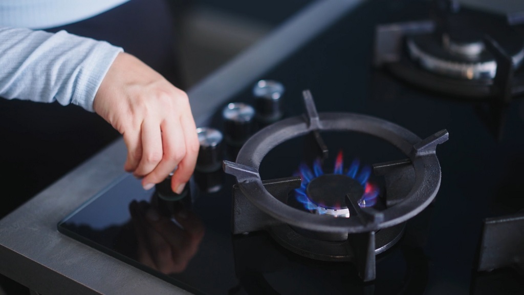 Close-up of a person adjusting the knob on a modern gas stove with a blue flame visible on the burner