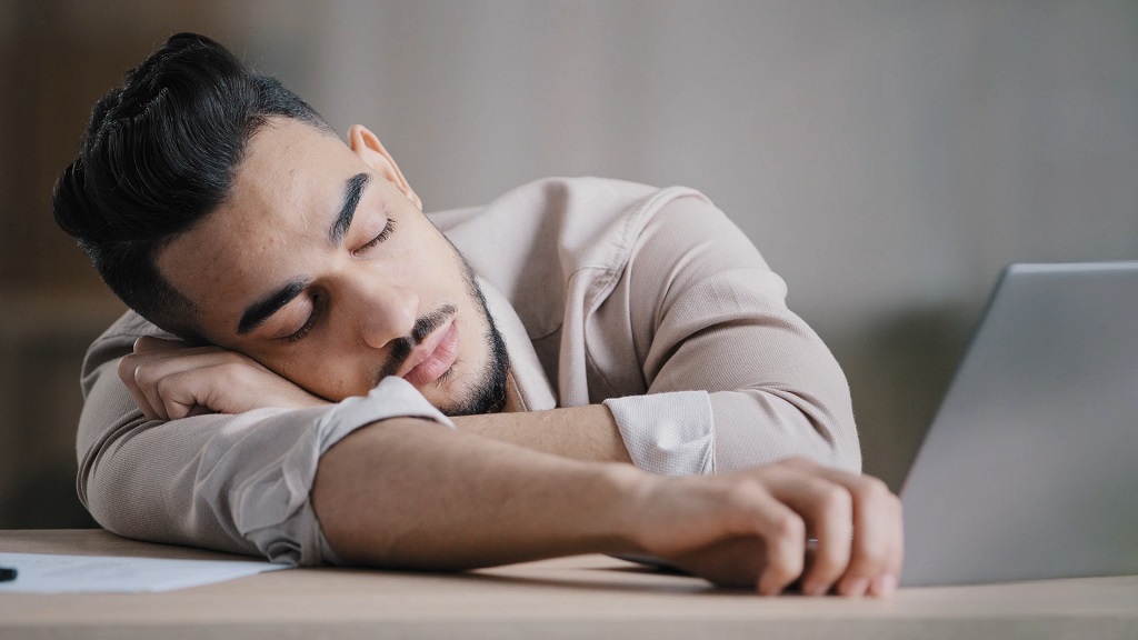 Tired man asleep at his desk next to a laptop, possibly affected by poor indoor air quality and high CO₂ levels