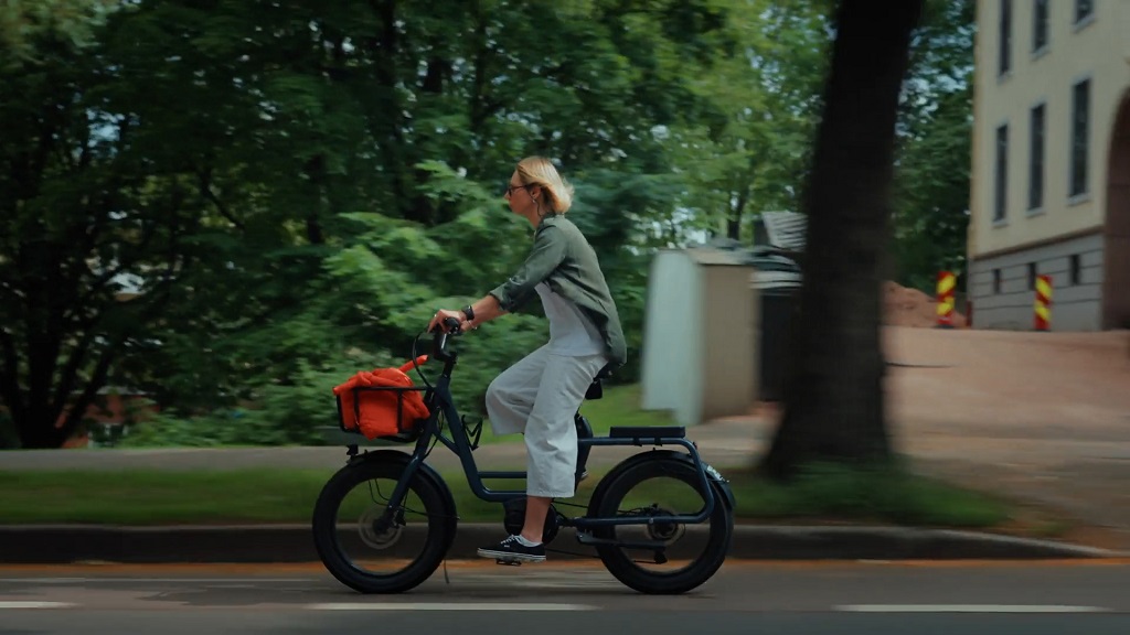 Woman riding an eBike with a front basket on a city street lined with trees and buildings