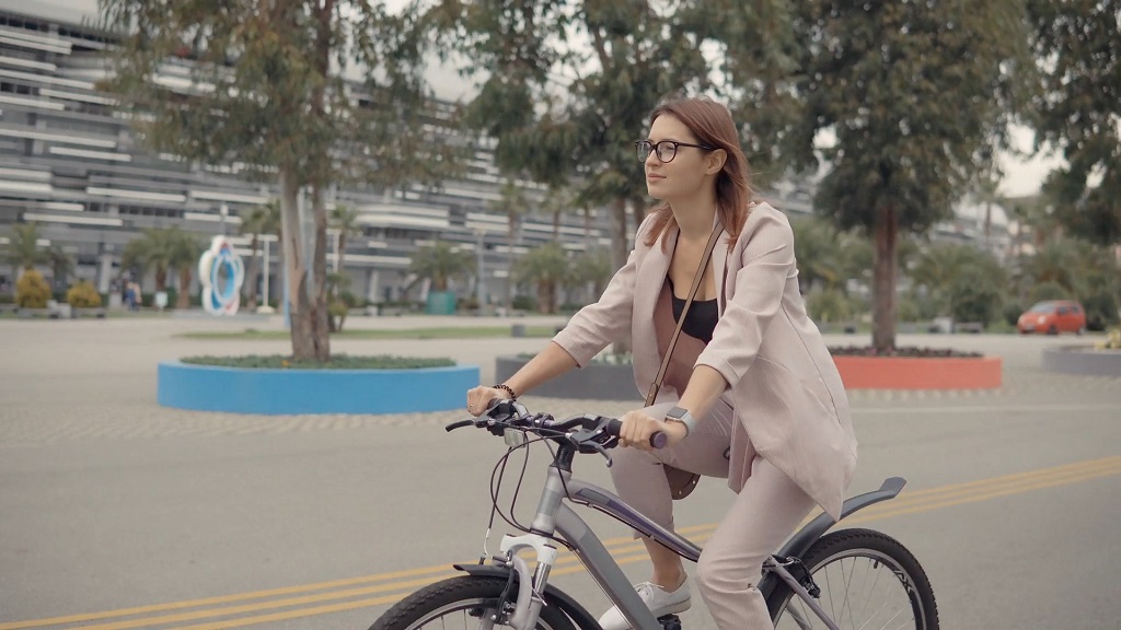 Businesswoman in a light suit riding an eBikes in an urban area with trees, modern buildings, and open space