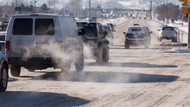 Cars release visible exhaust on a busy winter road, showing traffic-related emissions