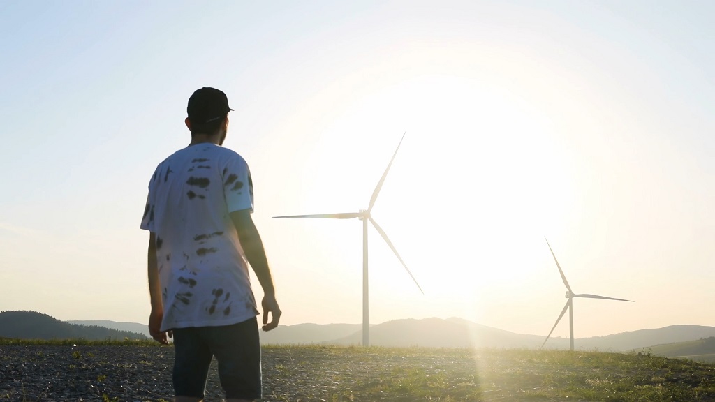 A man looking at wind turbines at sunset, symbolizing the potential of renewable energy for a sustainable future