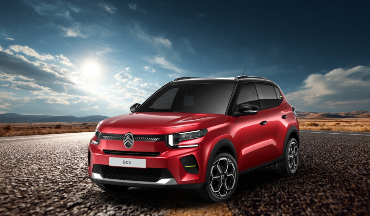 A red Citroën ë-C3 electric compact SUV parked on an open road under a scenic sky with distant hills
