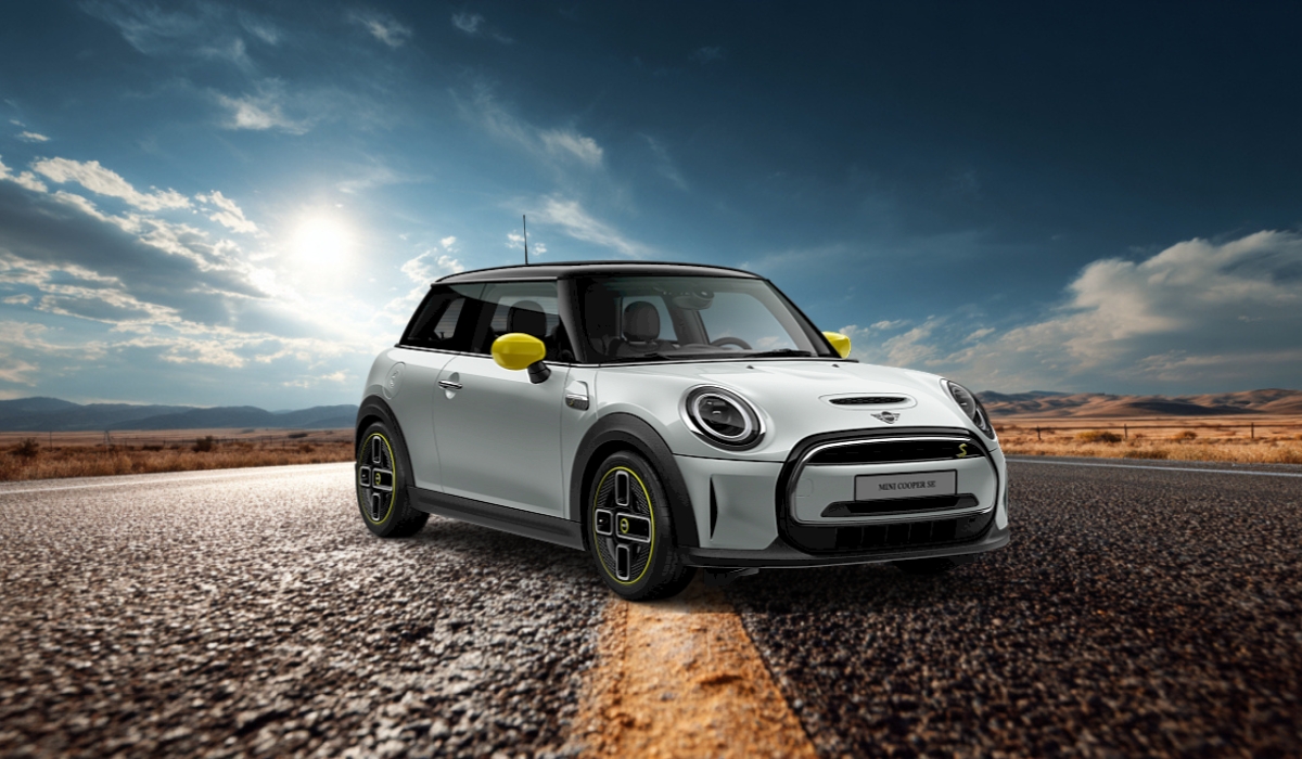 A white MINI Cooper Electric (SE) with yellow accents parked on an open road under a dramatic sky