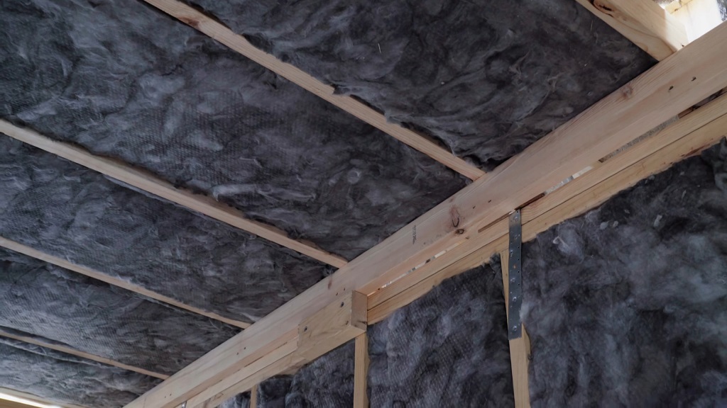 Fiberglass insulation installed between wooden joists in the ceiling of a construction site