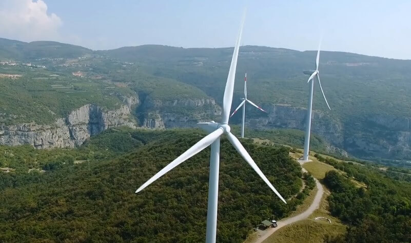 Wind turbines stand tall in the mountains beside a winding road
