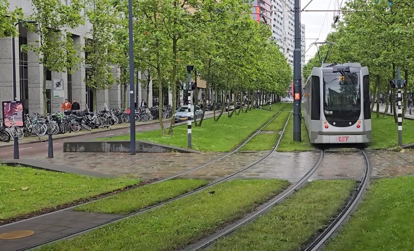 Amsterdam's urban landscape, showcasing a tram line amidst a vibrant green space, lined with parked bicycles and buildings
