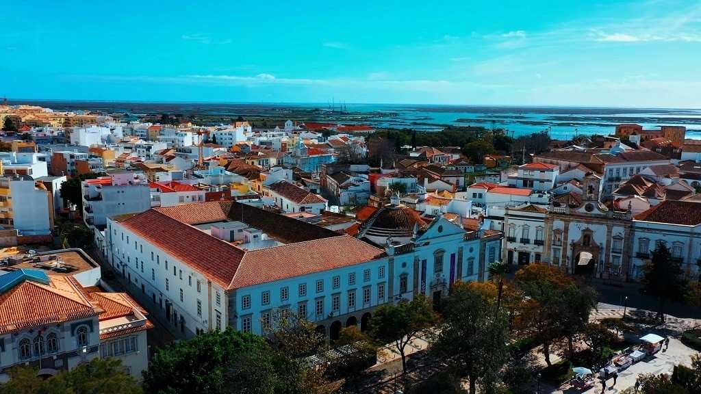 Aerial view of Faro, Portugal, featuring red-tiled rooftops, historic architecture, and the Atlantic coastline
