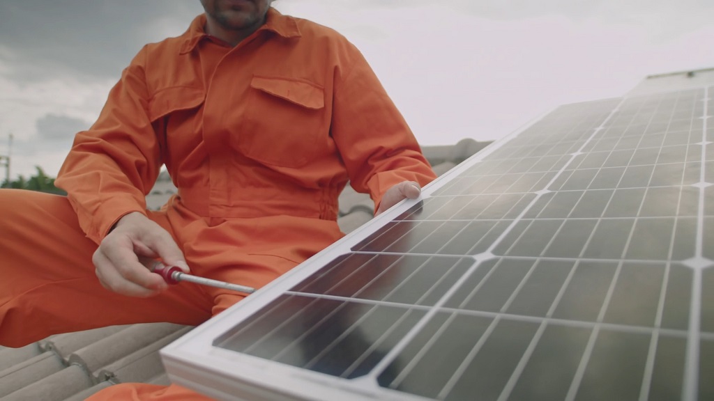 Technician in an orange uniform adjusting a solar panel with a screwdriver during a routine inspection