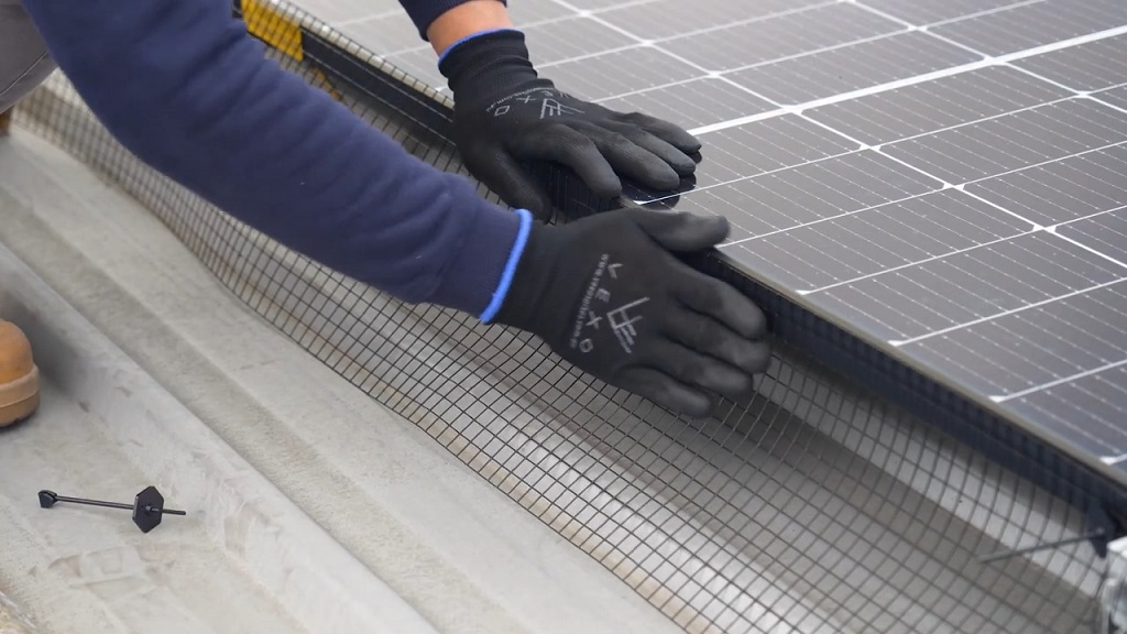 Worker in gloves installing a wire mesh barrier around solar panels to prevent birds from nesting underneath