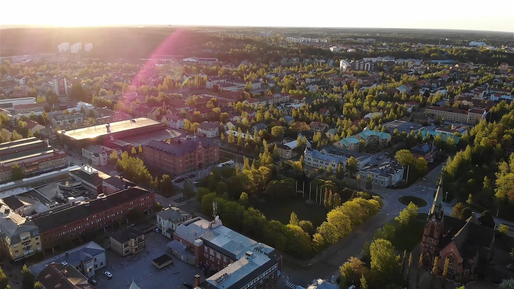 Drone view of Umeå, Sweden, at sunset with green trees, modern buildings, and warm sunlight