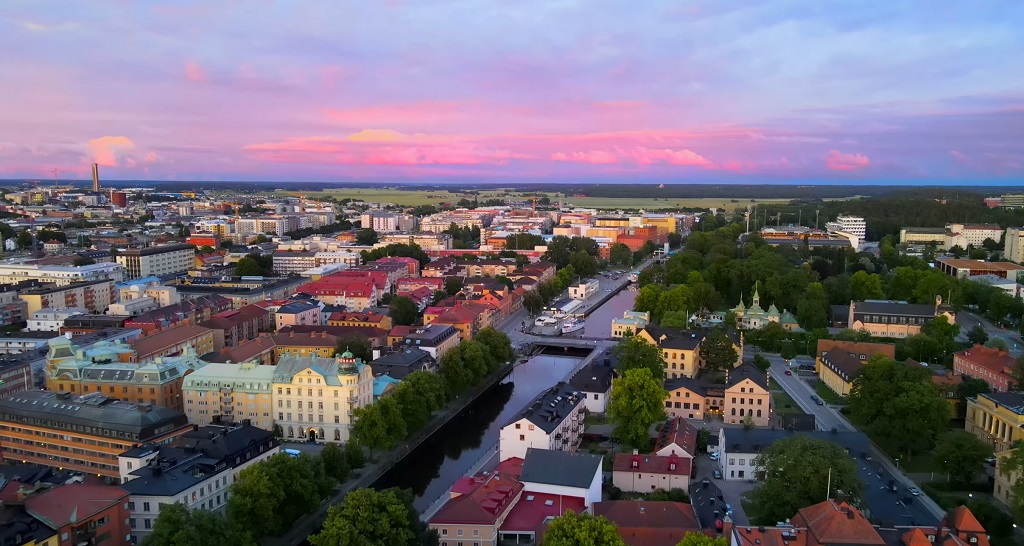 Aerial view of Uppsala, Sweden, with colorful buildings, river canal, and a vibrant sunset sky
