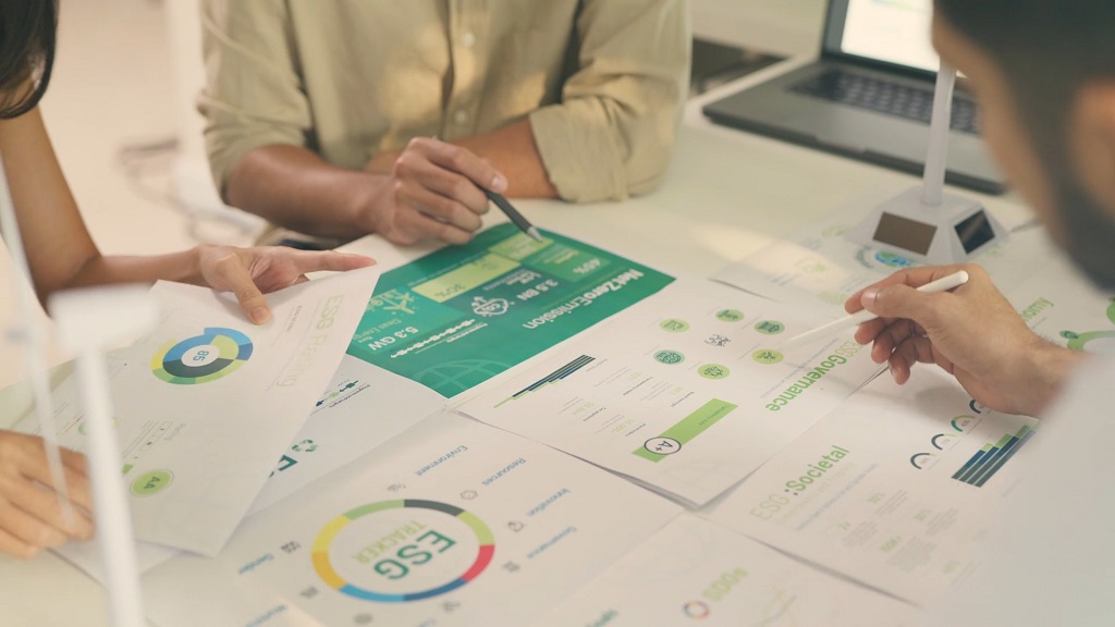 Team of professionals reviewing sustainability plans with wind turbine models and architectural blueprints in a modern office