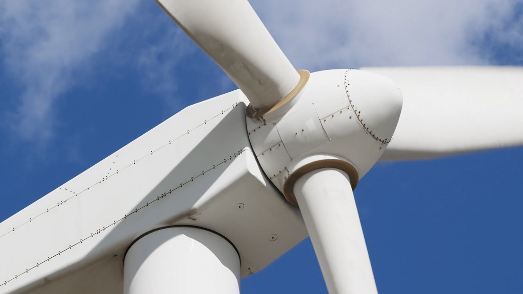 Close-up view of a horizontal-axis wind turbine hub and blade roots, highlighting the nacelle connection where mechanical rotation is transferred to internal drivetrain components