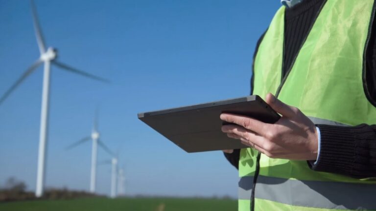 Engineer using a tablet to inspect horizontal axis wind turbines operating in an open field