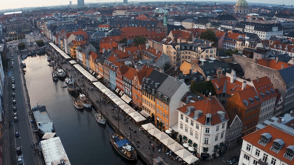 Aerial view of Copenhagen’s Nyhavn canal district with colorful historic buildings, outdoor cafés, and docked boats, showcasing the city’s architecture and energy-conscious urban design
