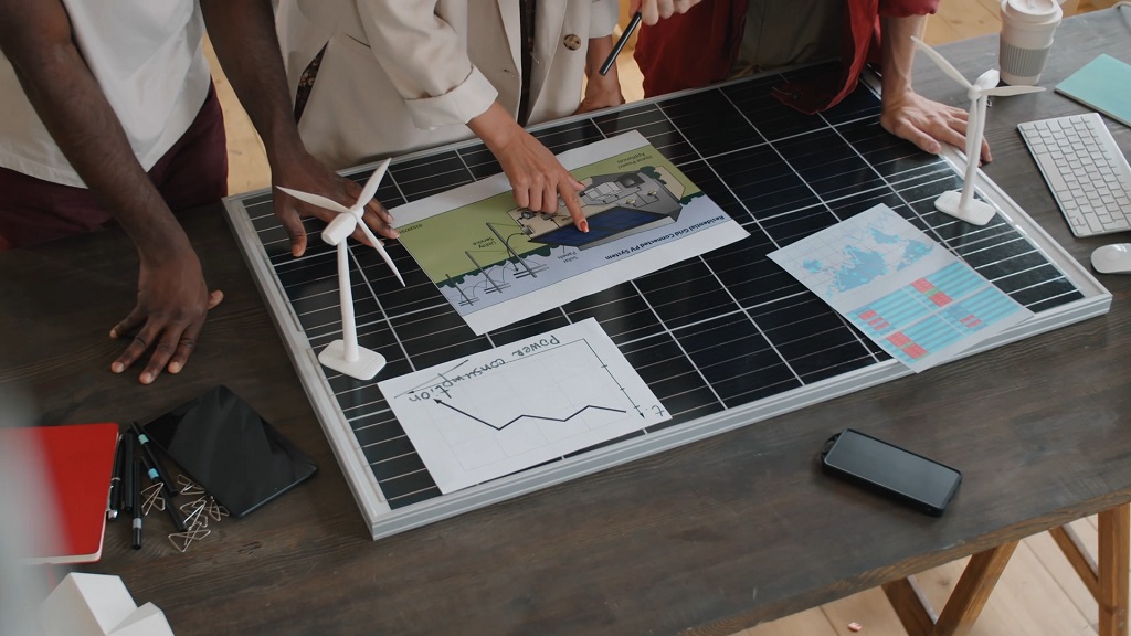 Business professionals analyzing solar energy charts and ESG data on a desk with wind turbine models and solar panel layouts
