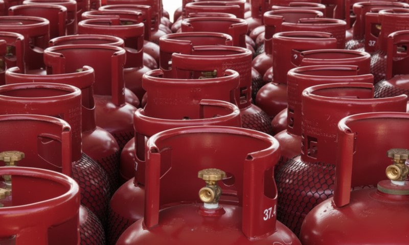 Many red gas cylinders are stacked closely together in a storage area