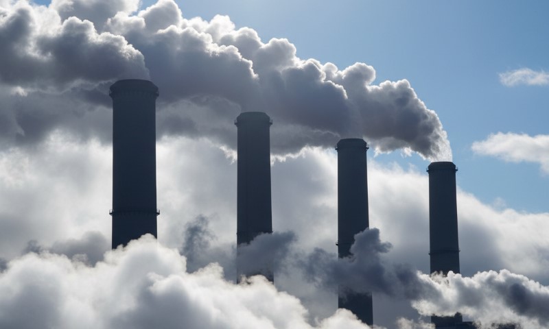 Four smokestacks emit dense clouds of smoke against a blue sky