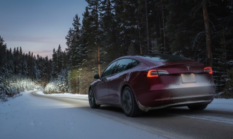 A red car is driving on a snowy, winding road through a dense forest