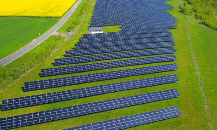 Aerial view of a solar farm in a green field, featuring rows of solar panels