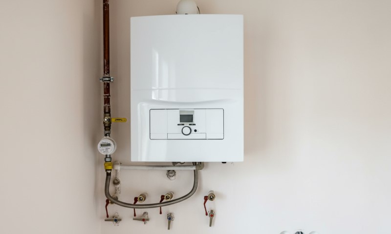 A modern white gas boiler is mounted on a light wall, with visible pipes and control panel