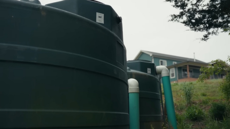 Large outdoor rainwater storage tanks connected to downpipes beside a residential home