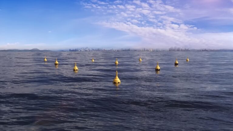 Wave energy converters floating offshore in rows with a coastal city visible in the distance