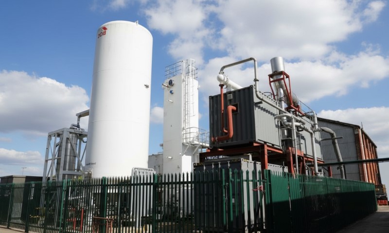 Industrial site featuring large white cylindrical tanks, metal structures, and a fenced perimeter