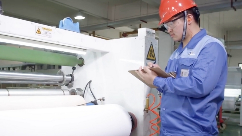 Factory worker inspects polymer backsheet material used on the rear side of solar panels