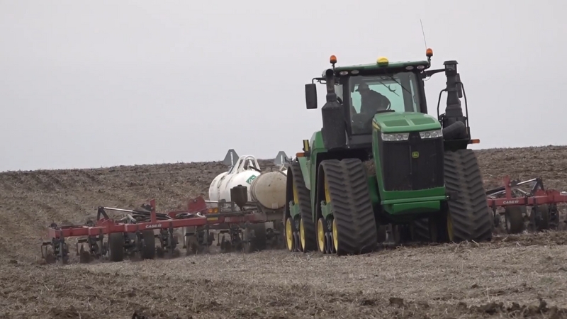 Farmer applies liquid ammonia fertilizer with a tractor and injection rig on a bare field