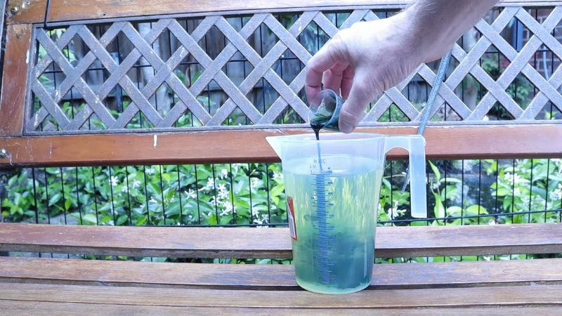 Person adds two-stroke oil into a measuring jug while preparing a 2 cycle oil mix ratio