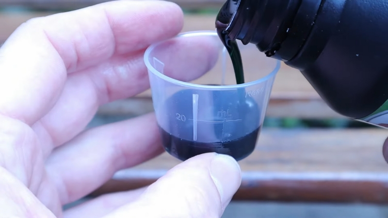 Person pours dark two-stroke oil into a small measuring cup for fuel mixing