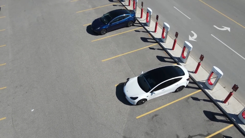 Two Tesla cars parked at Supercharger stations in a parking lot