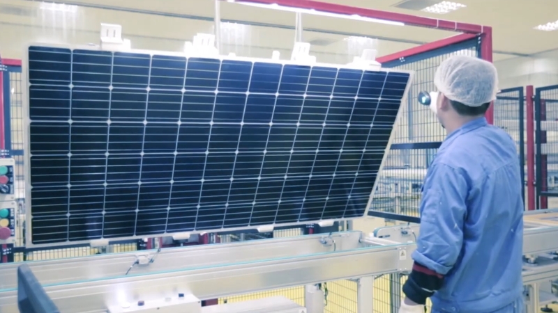 Worker inspecting a solar panel on a production line at a manufacturing facility
