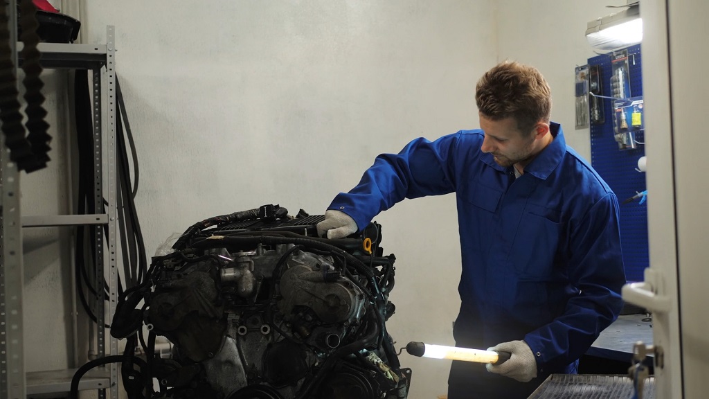 Mechanic examining a used engine component under workshop lighting