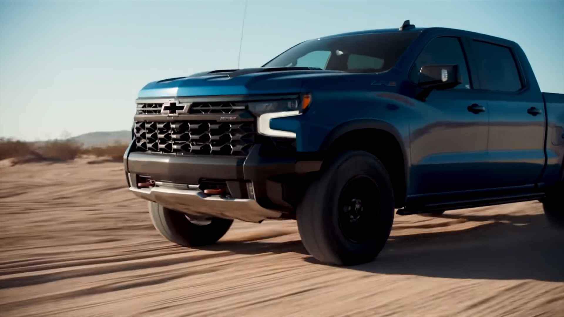 Pickup truck driving across a sandy landscape on an open road