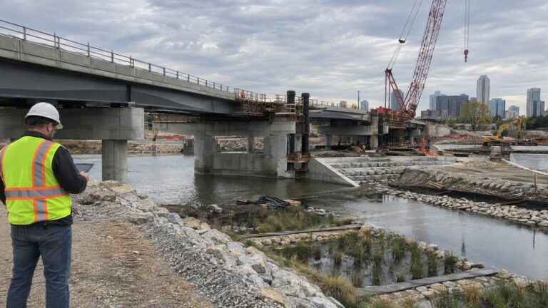 Engineer inspecting a bridge construction site beside a river.