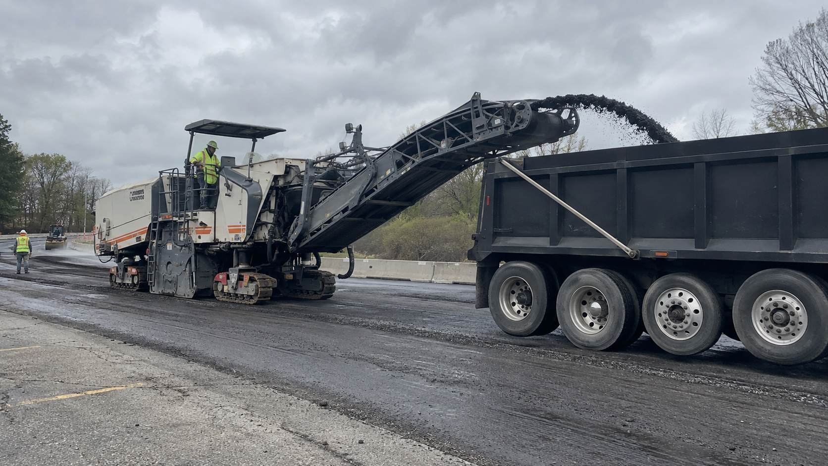 Road milling machine loading removed asphalt into a dump truck.